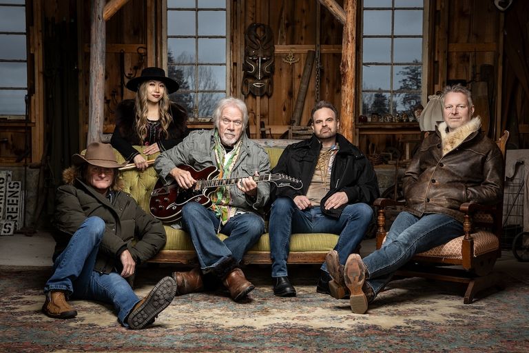 Canadian rock band Bachman-Turner Overdrive posing indoors, featuring Randy Bachman seated center on a couch holding a dark semi-hollow guitar.